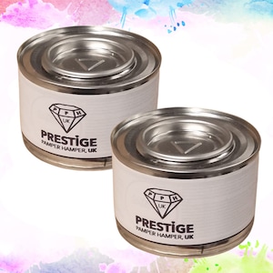 May include: Two silver metal cans with white labels. The labels feature a black diamond logo with the text "PH UK" inside. The text "PRESTIGE PAMPER HAMPER, UK" is printed below the logo.