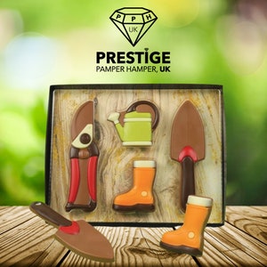 Peut inclure: Une boîte en bois remplie d'outils de jardin en chocolat. Les outils comprennent une paire de ciseaux, un arrosoir, une truelle et deux paires de bottes. La boîte est étiquetée "Prestige Pamper Hamper, UK".