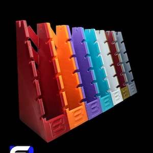 Pode incluir: Um conjunto de sete expositores de plástico coloridos, cada um com uma cor única, incluindo vermelho, laranja, roxo, azul, branco, vinho e cinza. Os expositores são inclinados e têm uma série de ranhuras para exibir itens. Cada expositor tem a letra "B" em relevo na parte inferior.