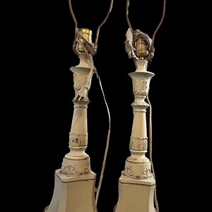 Może przedstawiać: Para białych ceramicznych lamp stołowych z złotymi akcentami i ozdobnymi detalami. Lampy mają klasyczny design i idealnie nadają się do dodania odrobiny elegancji do każdego pomieszczenia.