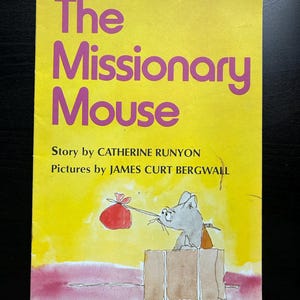 May include: A yellow book cover with the title "The Missionary Mouse" in pink lettering. The book cover features a watercolour illustration of a grey mouse with a red bag in its mouth, sitting in a brown suitcase.