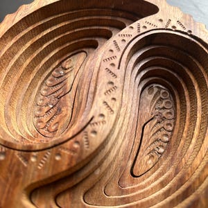 May include: A wooden bowl with intricate carvings in the shape of a yin yang symbol. The bowl is made of dark wood and has a smooth, polished finish.