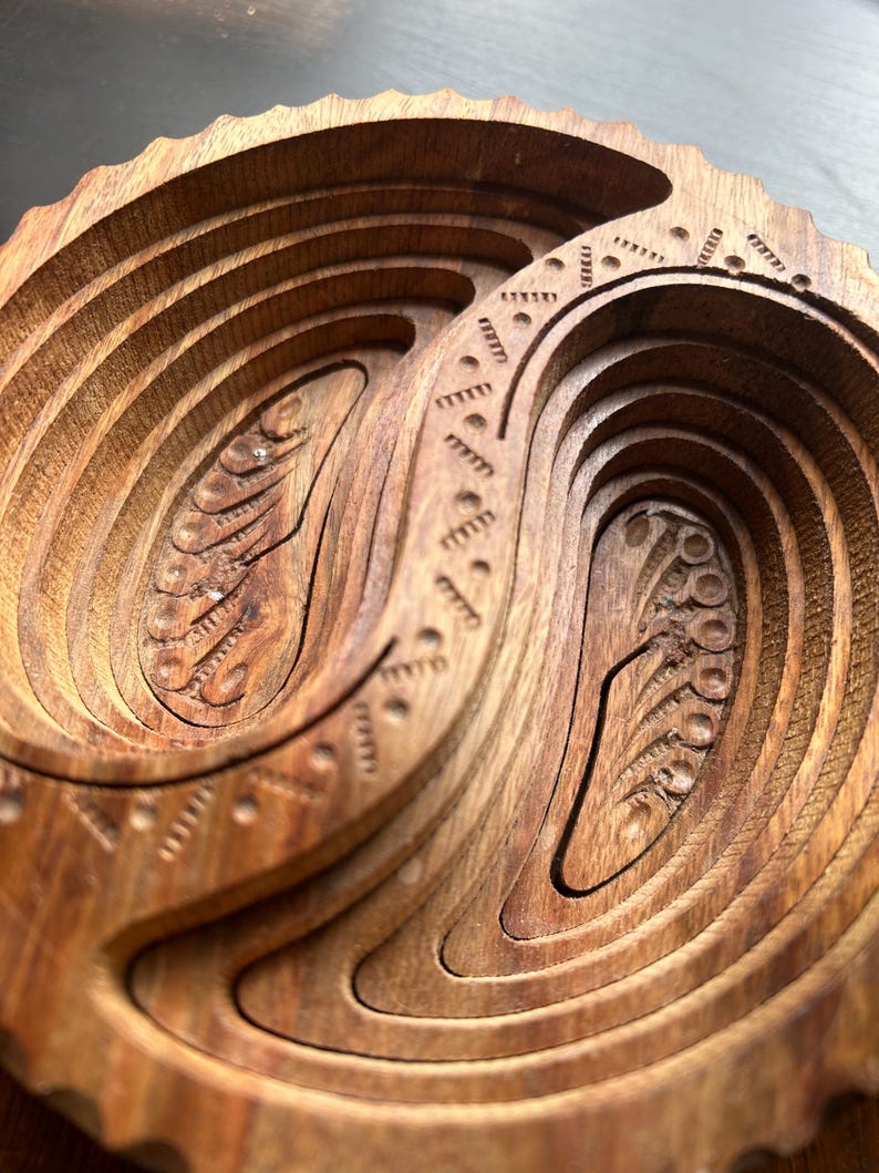 May include: A wooden bowl with intricate carvings in the shape of a yin yang symbol. The bowl is made of dark wood and has a smooth, polished finish.