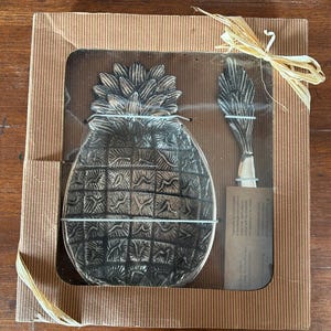 Könnte beinhalten: Dekoratives Ananas-Servierschalen- und Streuset-Set. Das silberfarbene Set wird in einer Pappschachtel mit Sichtfenster und Raffiabogen geliefert. Die Ananasschale hat einen Durchmesser von etwa 15 cm.