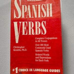 May include: A red book titled "Barron's Spanish Verbs" with the subtitle "Complete Conjugations in All Tenses". The book also states "Over 300 Most Commonly Used Spanish Verbs" and "Related Words and Expressions for Each Verb". The book is labelled as "#1 Choice in Language Guides".