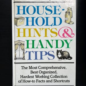 May include: A white book with the title "House-Hold Hints & Handy Tips" in colourful letters. The book is published by Reader's Digest and describes itself as "The Most Comprehensive, Best Organised, Hardest Working Collection of How-to Facts and Shortcuts".