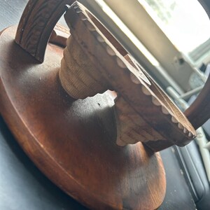 May include: A wooden, hand-carved, circular stand with a decorative, carved, arched top. The stand is made of dark brown wood and has a smooth, polished finish.
