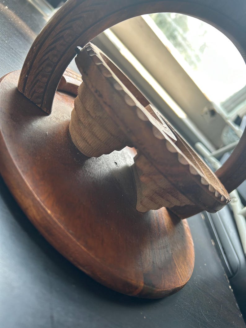 May include: A wooden, hand-carved, circular stand with a decorative, carved, arched top. The stand is made of dark brown wood and has a smooth, polished finish.