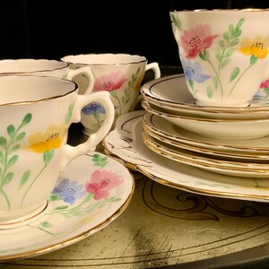 Puede incluir: Un juego de tazas de té y platillos vintage con flores y ribete dorado. Las tazas y los platillos presentan un delicado patrón floral con flores rosas, amarillas, azules y verdes.