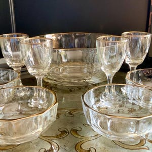 Puede incluir: Colección de fuentes de vidrio transparente con bordes dorados. El juego incluye copas de vino, cuencos pequeños y un cuenco grande. La cristalería está dispuesta sobre una bandeja decorativa.