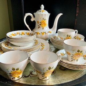 May include: A vintage tea set with a floral pattern of yellow roses on a white background. The set includes a teapot, teacups, saucers, and a serving plate.