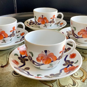 Puede incluir: Juego de cuatro tazas de té y platillos blancos con un diseño floral. Las tazas y los platillos presentan un patrón floral azul, naranja y dorado.