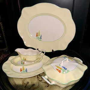 Può includere: Un set di quattro piatti da portata in porcellana vintage con sfondo giallo e bordo verde. I piatti presentano un motivo floreale con fiori blu, gialli e arancioni.
