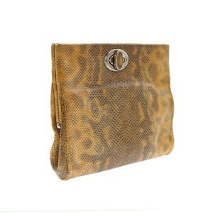 Peut inclure: Une pochette rectangulaire avec un motif peau de serpent dans les tons marron et beige. La pochette est dotée d'une fermeture à fermoir argenté. Le sac est plié en haut et a un fond arrondi.