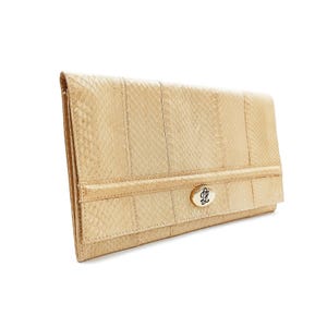 Könnte beinhalten: Eine beige Clutch mit Schlangenmuster. Die rechteckige Tasche hat einen Klappverschluss und einen goldfarbenen Verschluss mit einem verzierten Design. Die Clutch besteht aus einem strukturierten Material und hat ein segmentiertes Design.