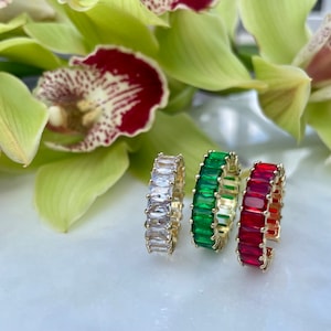 May include: Three gold rings with colourful baguette-shaped stones. The rings are white, green, and red.