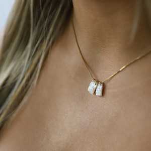 May include: A gold chain necklace with two white rectangular pendants. The pendants have a pearlescent finish.