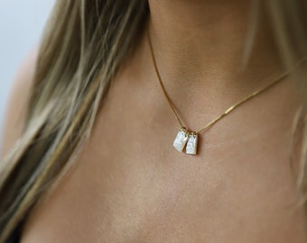 May include: A gold chain necklace with two white rectangular pendants. The pendants have a pearlescent finish.