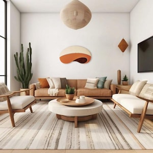 Op de afbeelding: Een moderne woonkamer met een bruin lederen bank, twee fauteuils en een ronde salontafel. De kamer heeft een grote cactus, een geweven hanglamp en een decoratief kunstwerk aan de muur met oranje en crèmekleur. Het tapijt heeft een streepjespatroon.