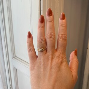 May include: A gold ring with a small diamond set in a twisted band. The ring is worn on the ring finger of a hand with brown nail polish.