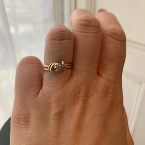 May include: A gold ring with a single, clear gemstone set in a twisted band.