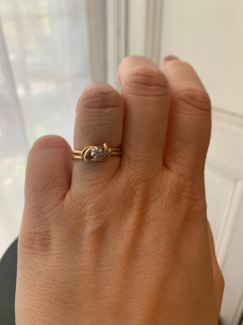 May include: A gold ring with a single, clear gemstone set in a twisted band.