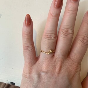 May include: A gold crescent moon ring with a small star detail. The ring is worn on the middle finger of a hand with nude nail polish.