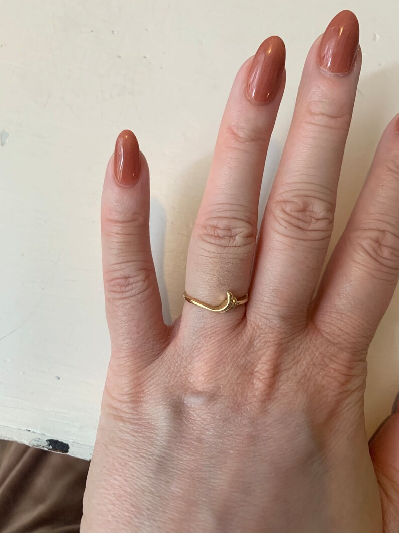 May include: A gold crescent moon ring with a small star detail. The ring is worn on the middle finger of a hand with nude nail polish.