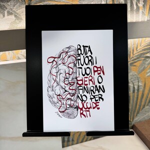 Op de afbeelding: Een zwartgelijste print met een gedetailleerde pen- en inkttekening van een hersen met rode lijnen. De rechterkant van de print heeft Italiaanse tekst in zwart en rood. De print wordt op een zwarte standaard gepresenteerd.
