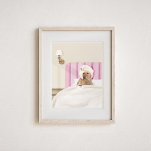 May include: A yellow Labrador Retriever wearing a white towel on its head sits in a pink bed with a white blanket and a cup of coffee. The dog is looking at the camera.