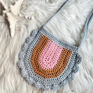 May include: A crocheted gray, pink, and brown bib with a scalloped edge and a long strap.