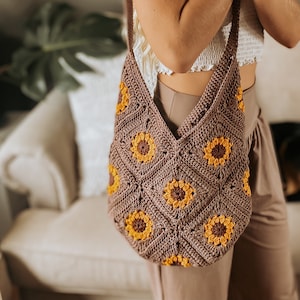 May include: A brown crocheted bag with a sunflower pattern. The bag has a long strap and is worn over the shoulder.