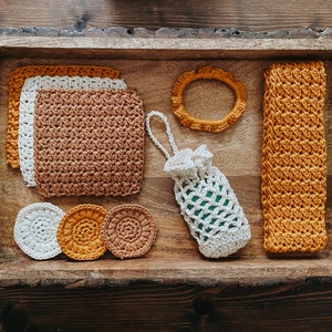May include: A wooden tray with a variety of crocheted items, including a round coaster, a long rectangular washcloth, a small pouch, and three round cotton rounds. The items are in shades of brown, white, and yellow.
