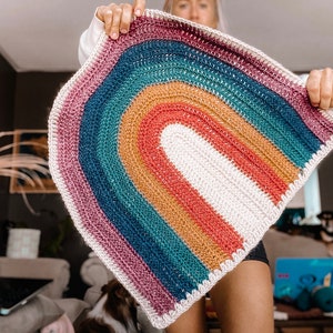 May include: A crocheted rainbow rug with a white center and a pink, teal, brown, and red outer edge.