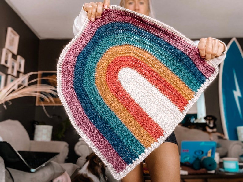 May include: A crocheted rainbow rug with a white center and a pink, teal, brown, and red outer edge.