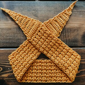 May include: Mustard yellow crochet top with a crisscross design. The handmade top features a textured stitch pattern and is displayed on a wooden surface. This item is a handmade piece of apparel.