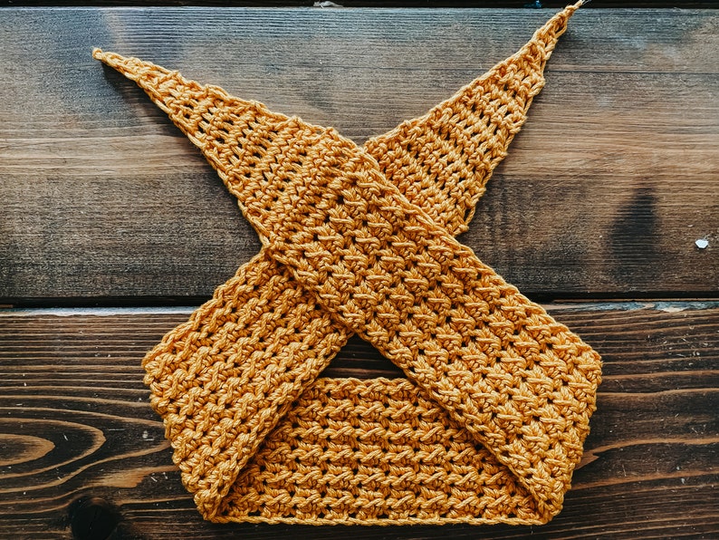 May include: Mustard yellow crochet top with a crisscross design. The handmade top features a textured stitch pattern and is displayed on a wooden surface. This item is a handmade piece of apparel.