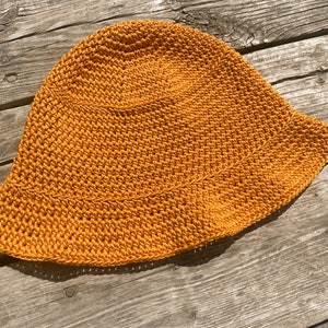 Op de afbeelding: Een gehaakte zonnehoed in een felle oranje kleur. De hoed heeft een brede rand en is gemaakt met een eenvoudig steekpatroon.