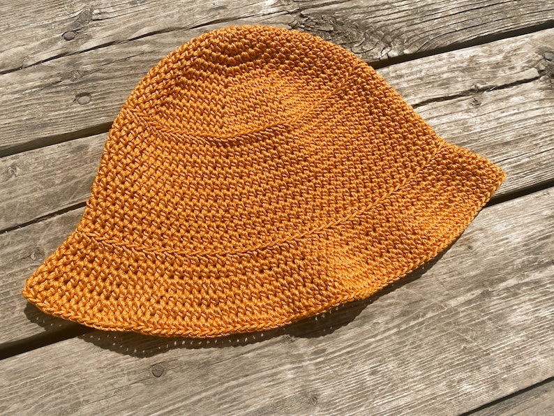 Op de afbeelding: Een gehaakte zonnehoed in een felle oranje kleur. De hoed heeft een brede rand en is gemaakt met een eenvoudig steekpatroon.