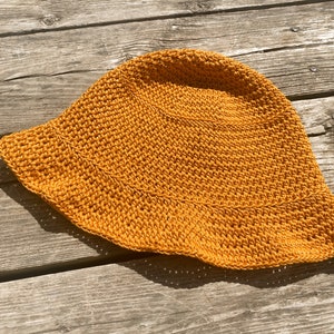 Op de afbeelding: Een gehaakte zonnehoed in een heldere gele kleur. De hoed heeft een brede rand en een ronde kroon.