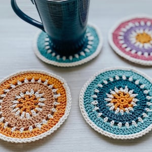Peut inclure: Quatre dessous-de-verre en crochet de différentes couleurs et motifs. Les dessous-de-verre sont ronds et ont un cercle central avec un cercle plus petit à l'intérieur. Les dessous-de-verre sont faits de différentes couleurs, notamment le bleu, le vert, le violet et l'orange.