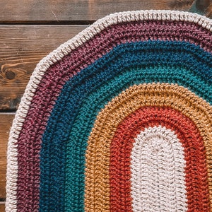 May include: A colorful crocheted oval rug with a rainbow pattern in shades of purple, teal, mustard yellow, red, and white.