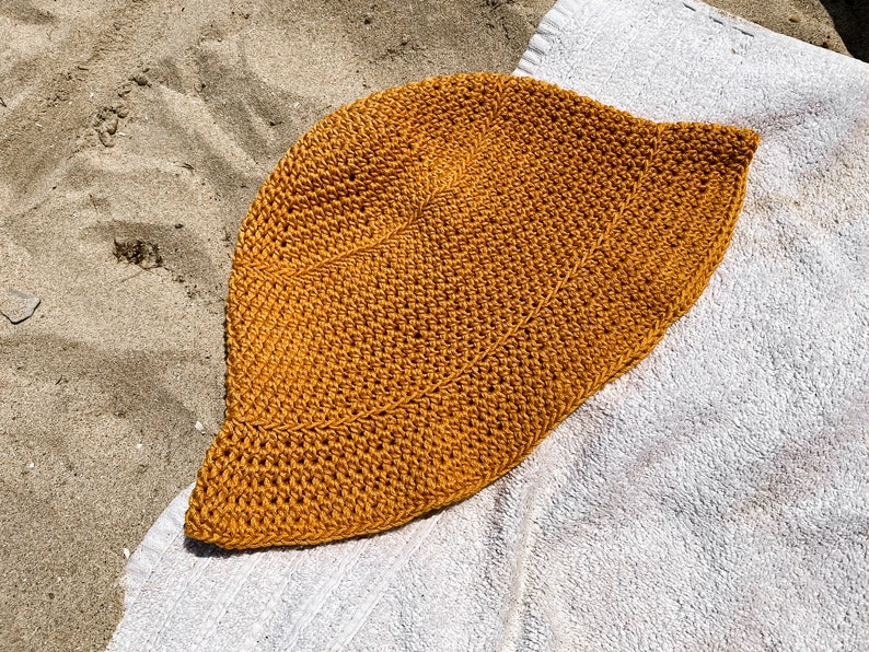 Op de afbeelding: Een gehaakte zonnehoed in een mosterdgele kleur. De hoed is gemaakt van dik, getextureerd garen en heeft een brede rand.