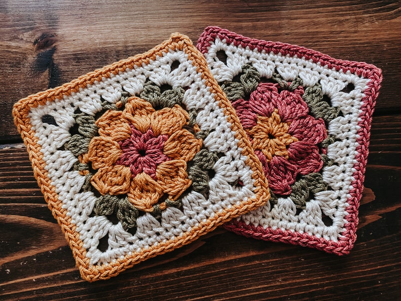 K&ouml;nnte beinhalten: Zwei quadratische H&auml;keluntersetzer mit Blumendesigns. Ein Untersetzer zeigt eine Blume in Orange- und Rosat&ouml;nen mit gr&uuml;nen Bl&auml;ttern und einem cremefarbenen Hintergrund. Der andere Untersetzer hat ein &auml;hnliches Design, aber mit rosa Rand und Blume.