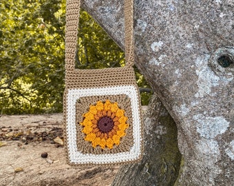 Op de afbeelding: Een gehaakte zonnebloem crossbody tas met een bruine band en een witte rand rond het zonnebloemontwerp.