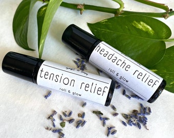May include: Two small black roller bottles with white labels. The labels read "tension relief roll & glow" and "headache relief roll & glow". Dried lavender flowers are scattered around the bottles.