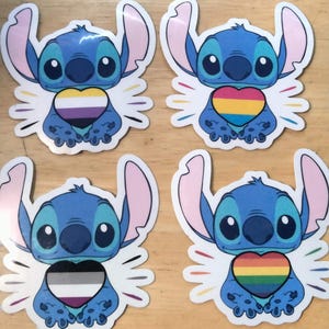 May include: Four blue Stitch character stickers with different colored hearts. The hearts are yellow, orange, and red with black stripes, black and white with a purple stripe, and a rainbow.