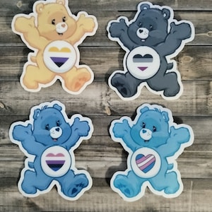 May include: Four Care Bear stickers with different colored fur and hearts featuring different pride flags. The bears are yellow, black, blue, and blue. The hearts feature the bisexual, asexual, transgender, and pansexual pride flags.