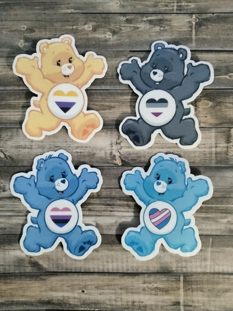 May include: Four Care Bear stickers with different colored fur and hearts featuring different pride flags. The bears are yellow, black, blue, and blue. The hearts feature the bisexual, asexual, transgender, and pansexual pride flags.
