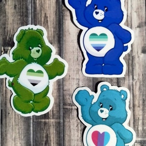 May include: Three Care Bear stickers with different colored fur and hearts. The first sticker is green with a green, gray, and white heart. The second sticker is blue with a blue, green, and white heart. The third sticker is teal with a pink, purple, and blue heart.